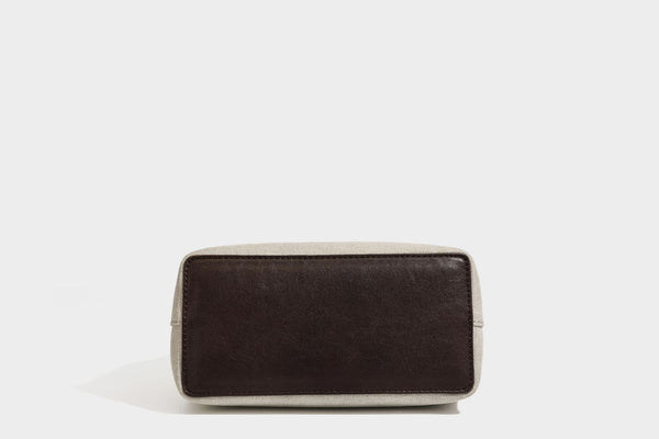 Small structured beige canvas top-handle bag with dark brown leather-look trim, silver turn-lock hardware, and detachable