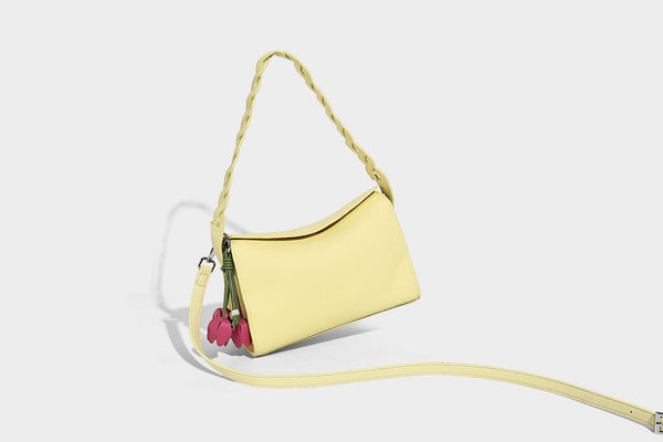 Small structured pebbled-finish shoulder bag with braided top handle, detachable crossbody strap, floral tassel charm, and