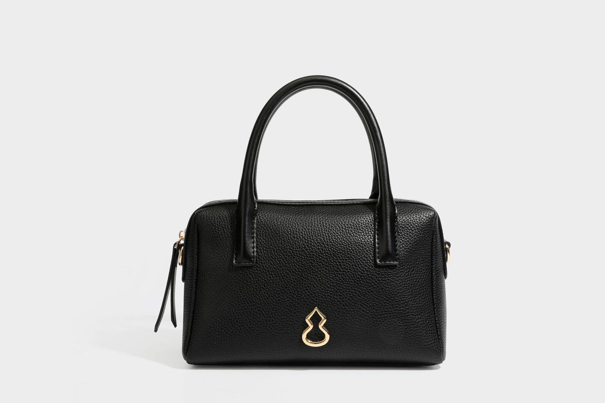 Small structured pillow satchel bag with pebbled leather-look finish, dual rolled top handles, gold-tone gourd emblem, and