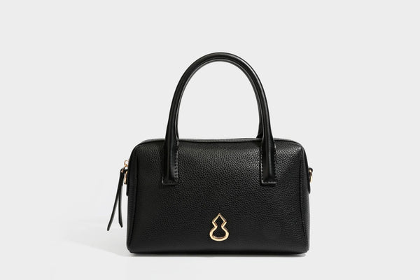 Small structured pillow satchel bag with pebbled leather-look finish, dual rolled top handles, gold-tone gourd emblem, and