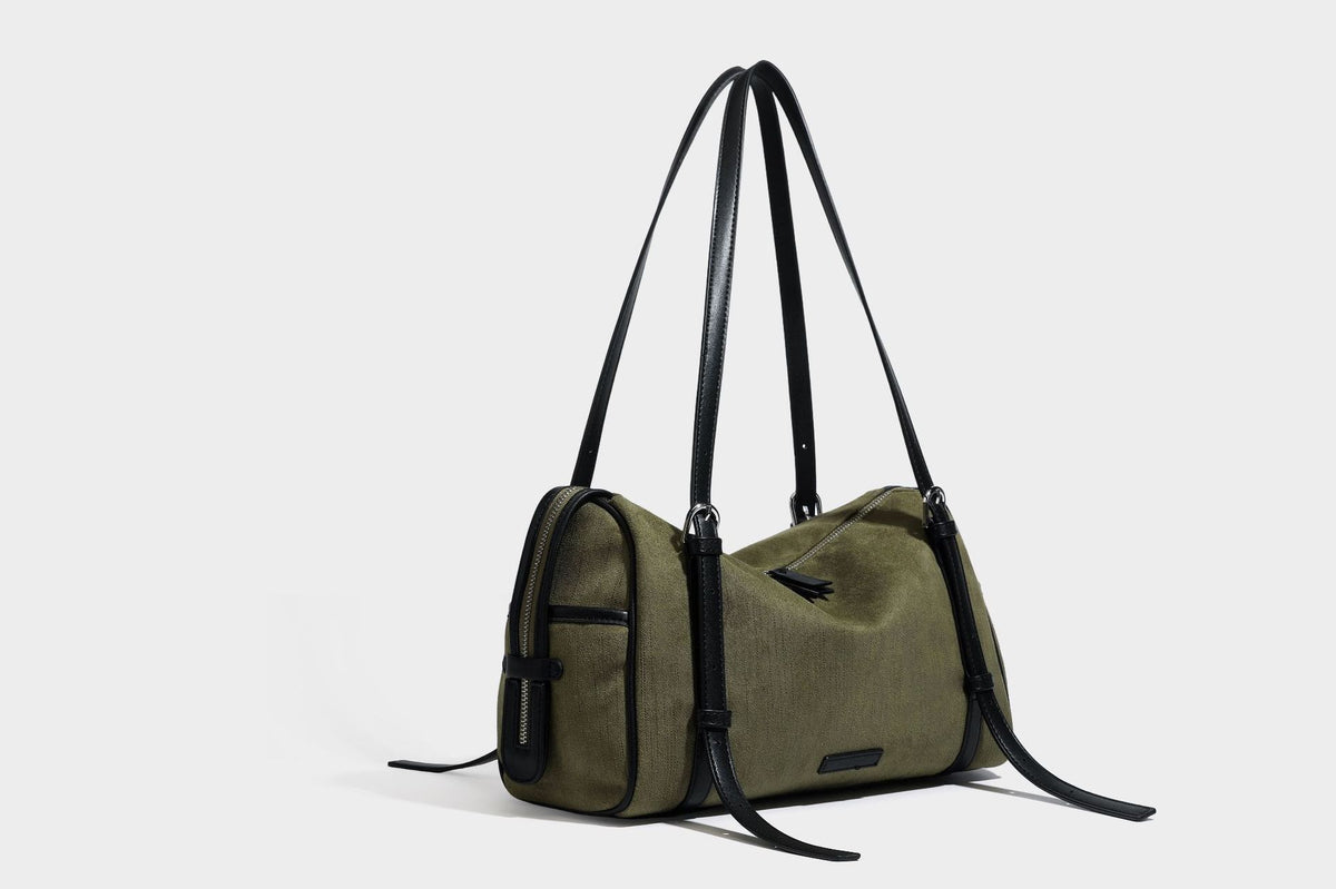 Olivgrüne Canvas-Schultertasche in Zylinderform mit schwarzen Trägern in Lederoptik, Reißverschluss oben und silberfarbenen Metallbeschlägen, Detailansicht