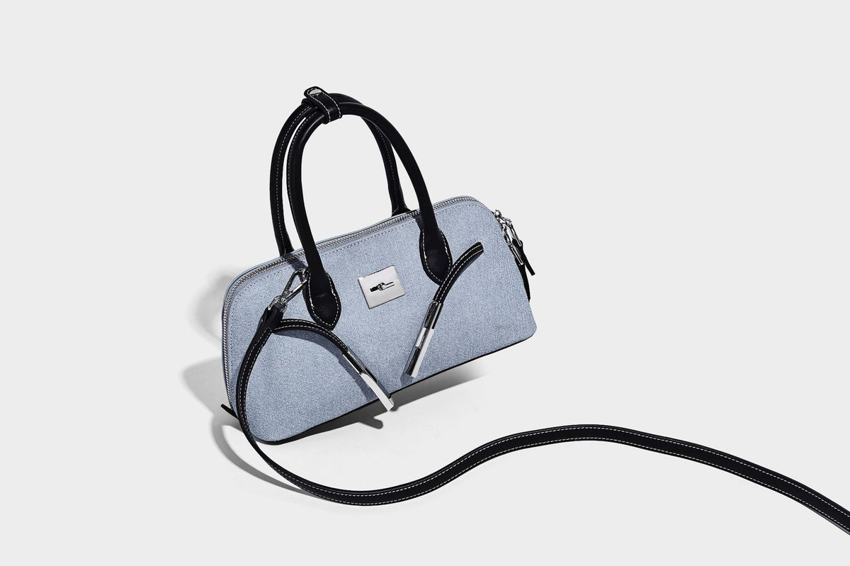 Compact structured satchel in light blue denim-look fabric with black leather-look trim, silver turn-lock closure, rolled