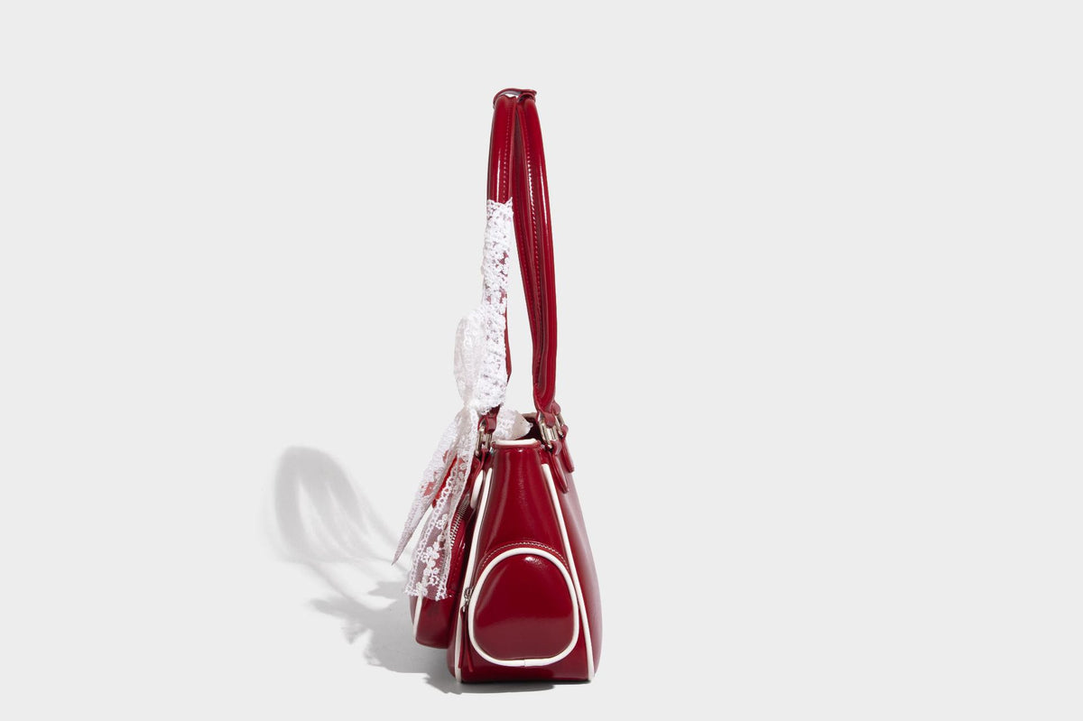 Kleine, formstabile, glänzende Schultertasche mit weißer Paspelierung, Spitzenschleife und Anhänger mit roter Perle, seitlichen Reißverschlusstaschen und silberfarbenem