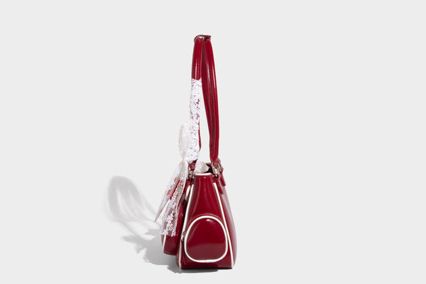 Kleine, formstabile, glänzende Schultertasche mit weißer Paspelierung, Spitzenschleife und Anhänger mit roter Perle, seitlichen Reißverschlusstaschen und silberfarbenem