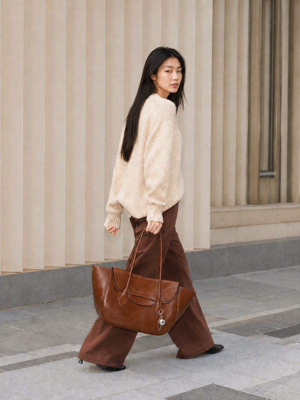 Large winged leather-look tote bag with single arched handle, stitched flap-front panel, and silver ball charm in cognac