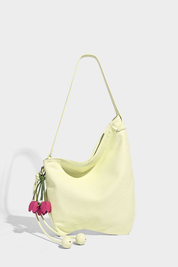 Slouchy hobo shoulder bag in pale yellow with slim strap, drawstring bead closure, and pink tulip floral charm, detail view