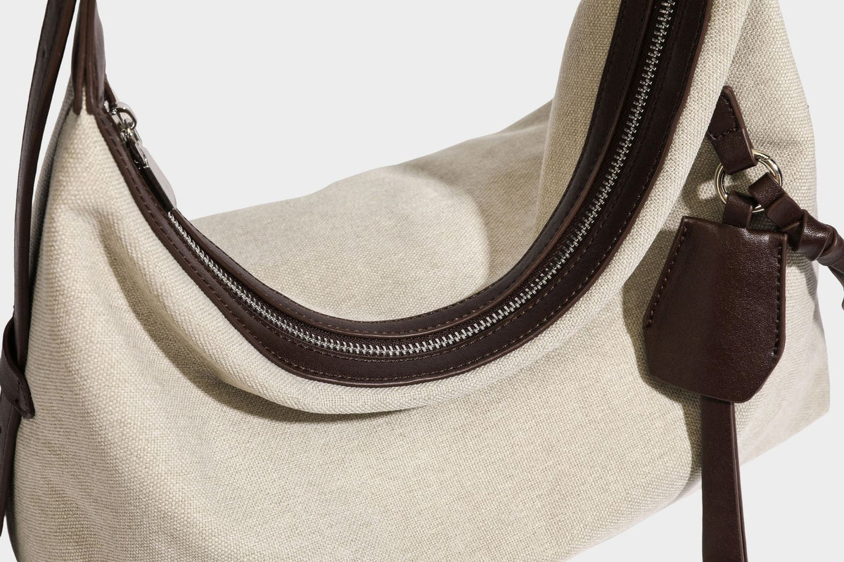 Lässige Hobo-Schultertasche aus haferfarbenem Canvas mit dunkelbraunen Besätzen in Lederoptik, silberfarbenem Reißverschluss und langem, verstellbarem
