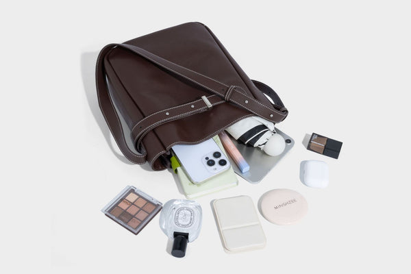 Structured dark brown leather-look bucket bag with white contrast stitching, front wraparound belt buckle strap, and long