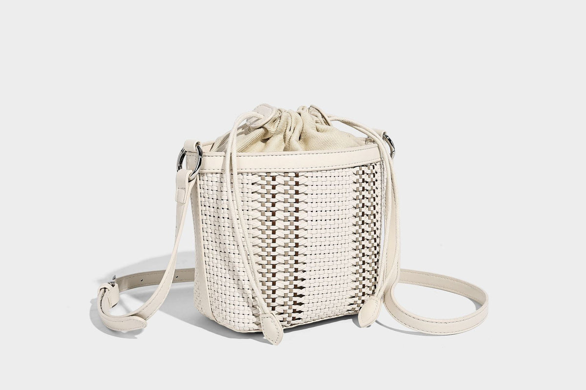 Small woven bucket bag with drawstring top, braided handle, detachable crossbody strap, and silver-tone ring hardware, detail