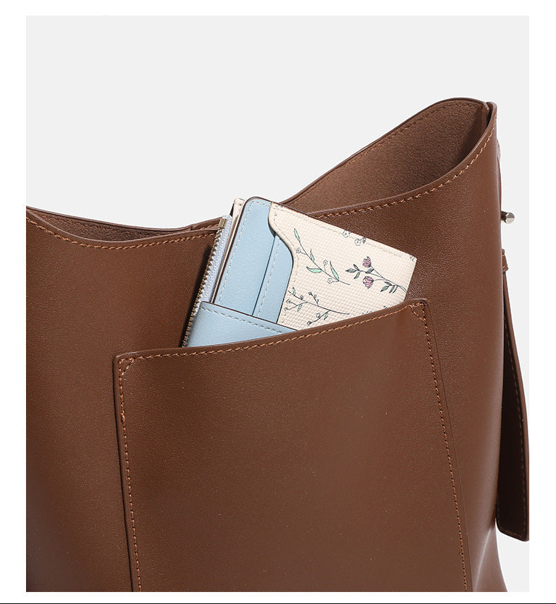 Smooth leather-look bucket bag with long flat shoulder strap, open top, gold-tone hardware, and decorative rabbit charm