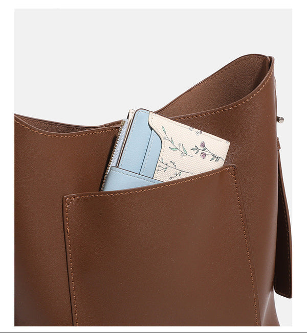 Smooth leather-look bucket bag with long flat shoulder strap, open top, gold-tone hardware, and decorative rabbit charm