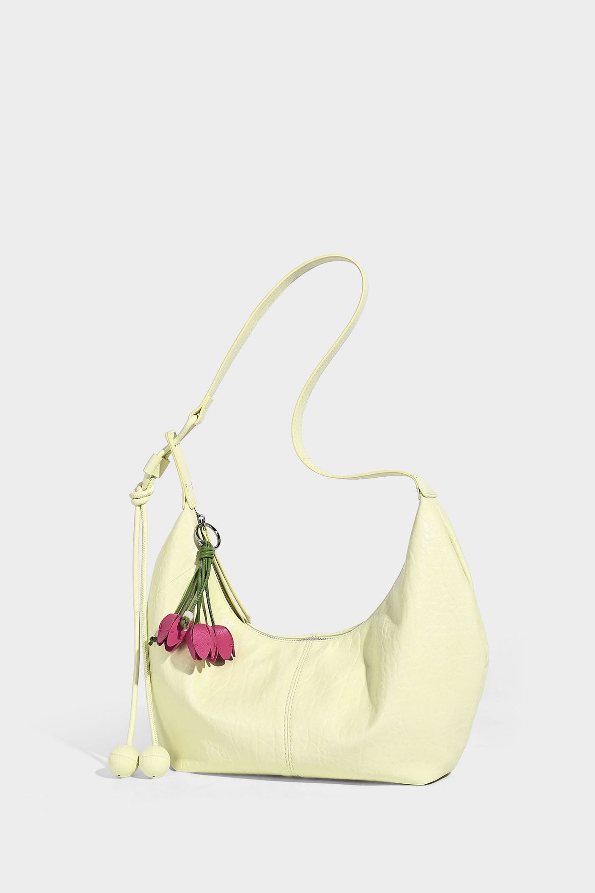Slouchy crescent half-moon shoulder bag in pink pebbled textured finish with floral charm and knotted side detail, detail