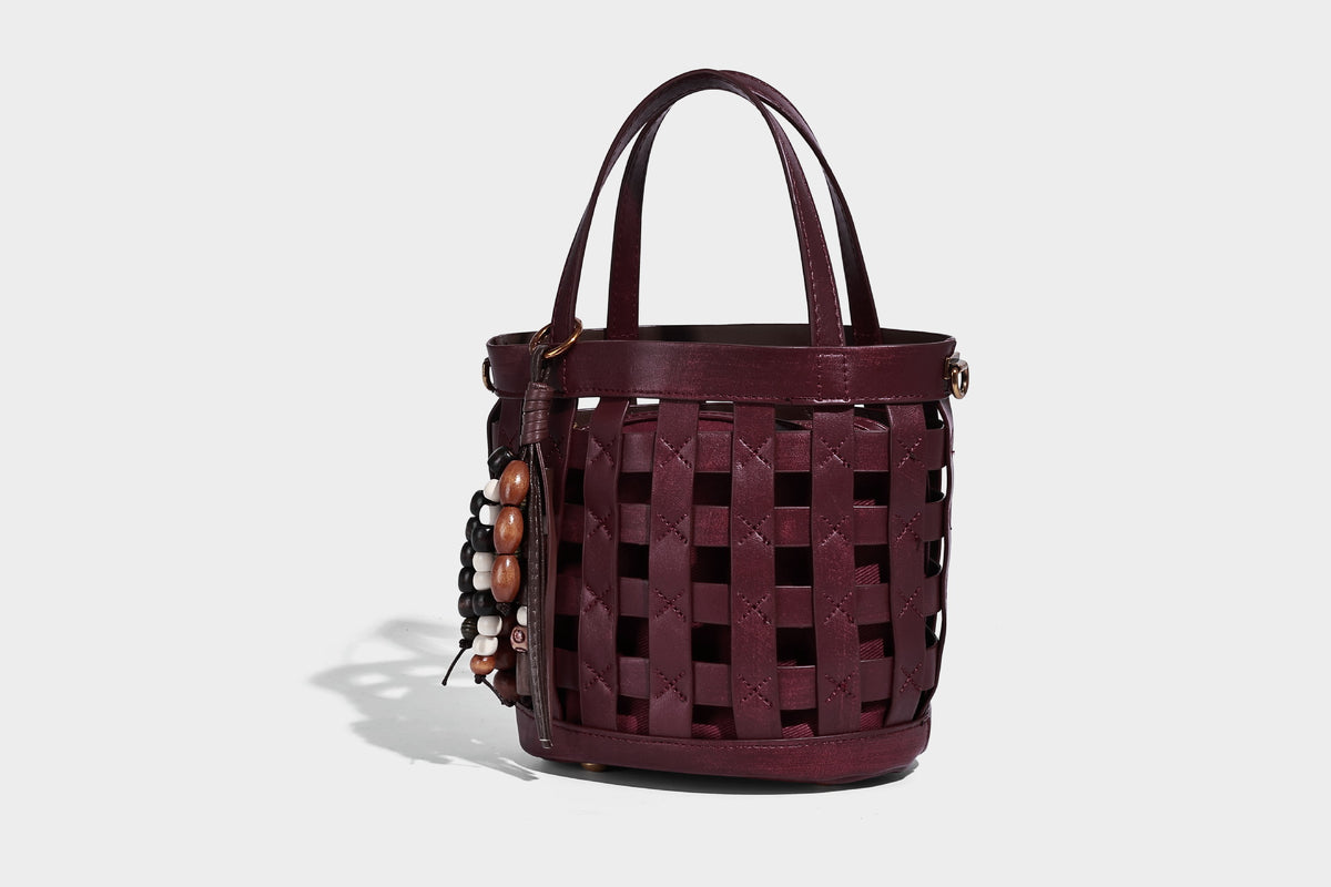 Small woven lattice bucket bag in brown leather-look finish with beaded tassel charm, dual top handles, and detachable