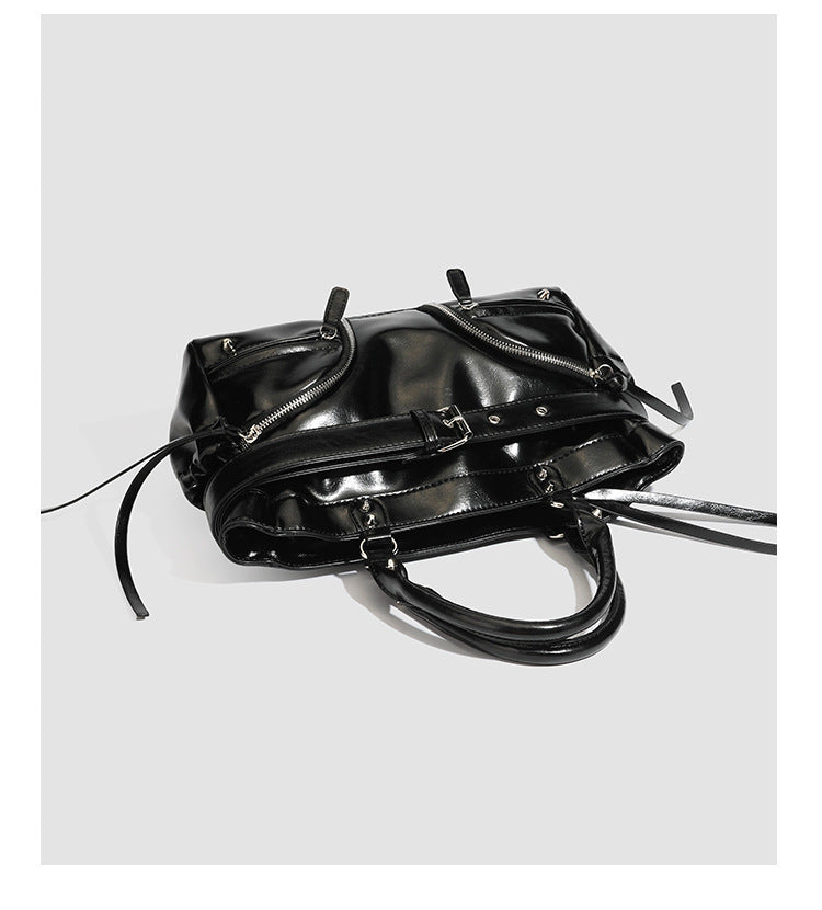 Black glossy structured tote bag with rivet and buckle detail, dual top handles, and detachable shoulder strap, detail view