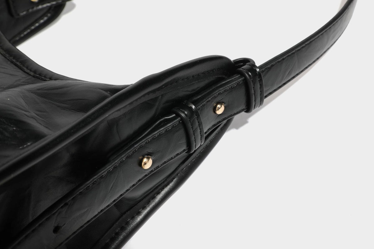 Strukturierte, trapezförmige Schultertasche aus glänzender, geknautscht wirkender Lederoptik mit goldfarbenen Beschlägen auf der Vorderseite und langem, verstellbarem