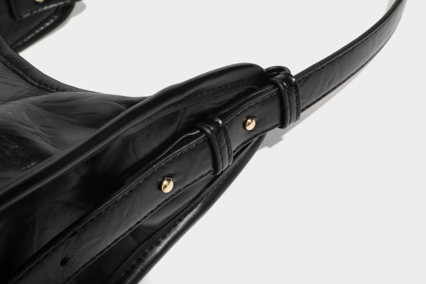 Strukturierte, trapezförmige Schultertasche aus glänzender, geknautscht wirkender Lederoptik mit goldfarbenen Beschlägen auf der Vorderseite und langem, verstellbarem