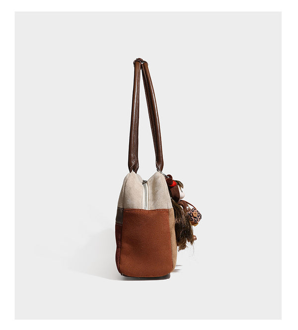Boxy patchwork suede-look shoulder tote in tan, beige, rust, and brown panels with double brown straps and hanging doll