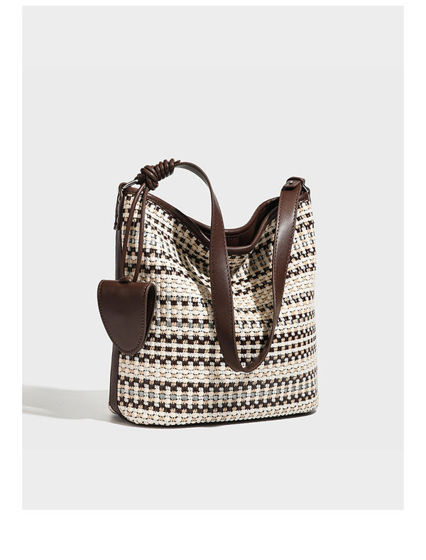 Woven stripe bucket shoulder bag in cream and dark brown with leather-look trim, knotted adjustable strap, and small shield