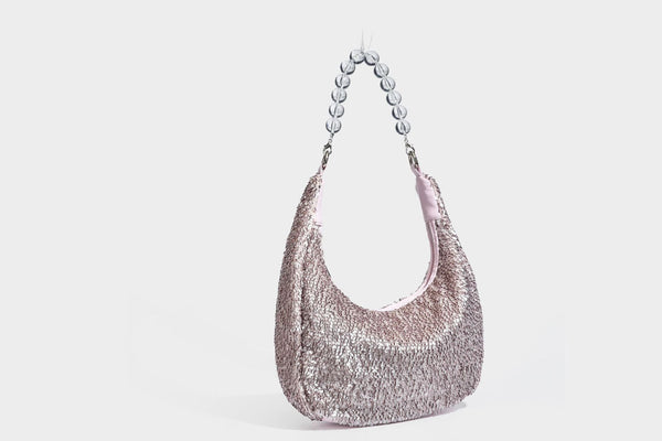 Kleine sichelförmige Schultertasche mit vollständig mit silberfarbenen Pailletten besetzter Außenseite, transparentem Henkel aus kugelförmigen Perlen und Reißverschluss in Silberoptik