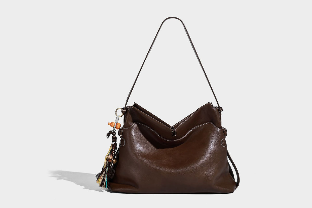 Large slouchy leather-look hobo tote bag with open top, adjustable shoulder strap, and colorful tassel bead charm, detail