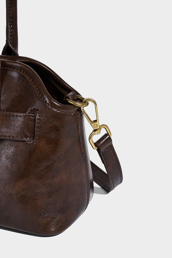 Strukturierte dunkelbraune Henkeltasche mit Öl-Wachs-Finish, vorderer Gürtelschnalle, goldfarbenen Beschlägen und zwei Tragegriffen, Detailansicht