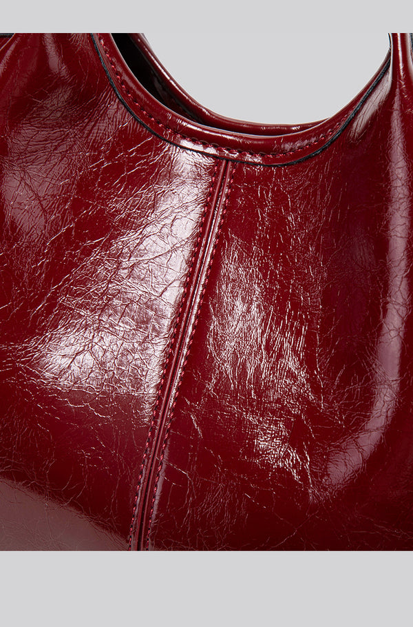 Structured crinkle-gloss top-handle satchel in deep burgundy with antique gold lock charm and detachable shoulder strap