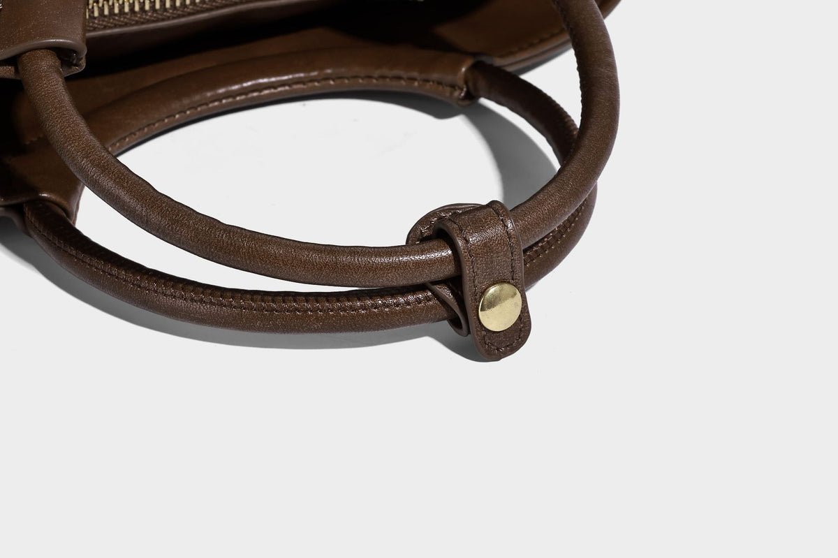 Small woven-panel bucket bag with circular ring handles, beaded tassel charm, and detachable crossbody strap in brown, detail