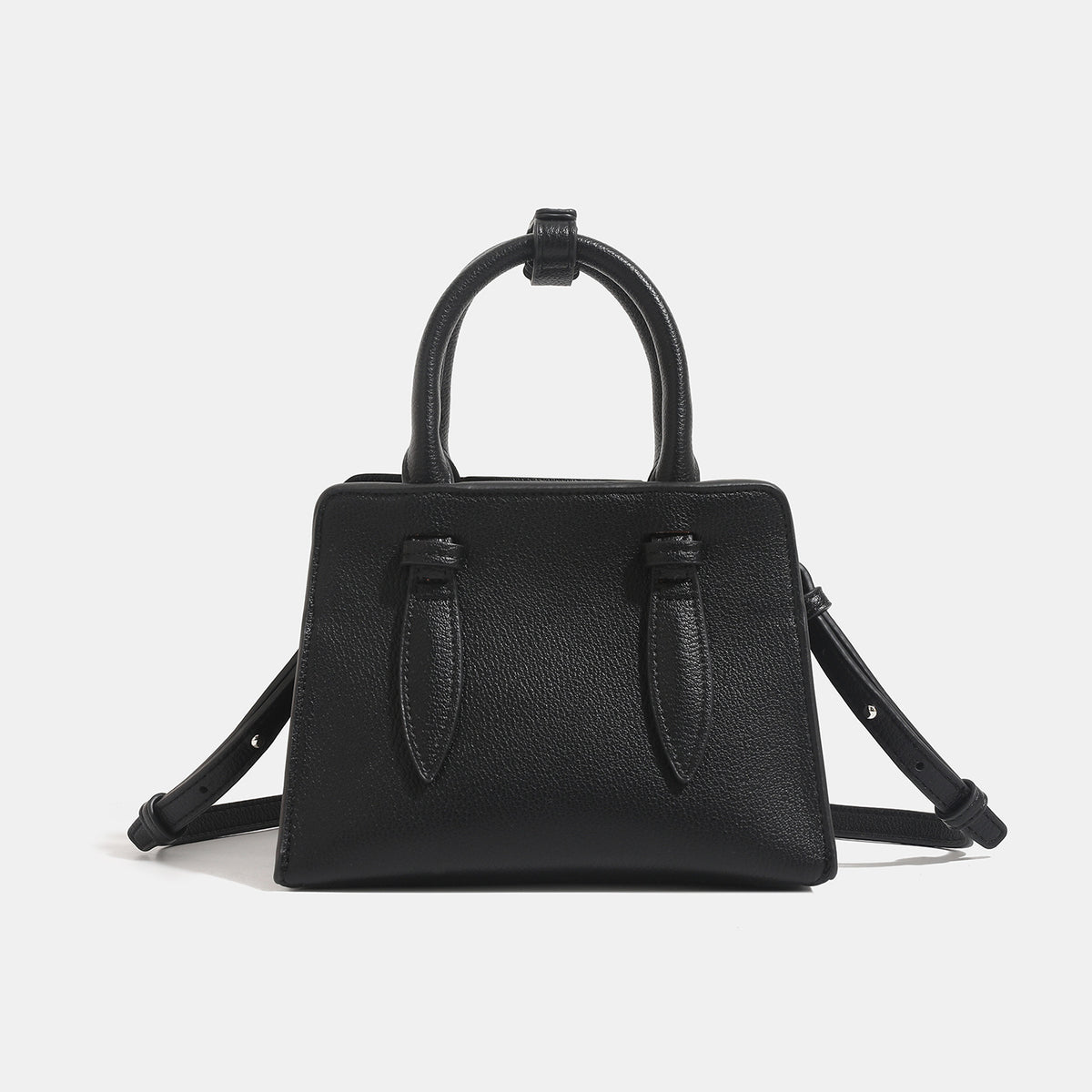 Small structured trapezoid top-handle bag in pebbled matte finish with decorative strap tabs, twin knotted handles, and