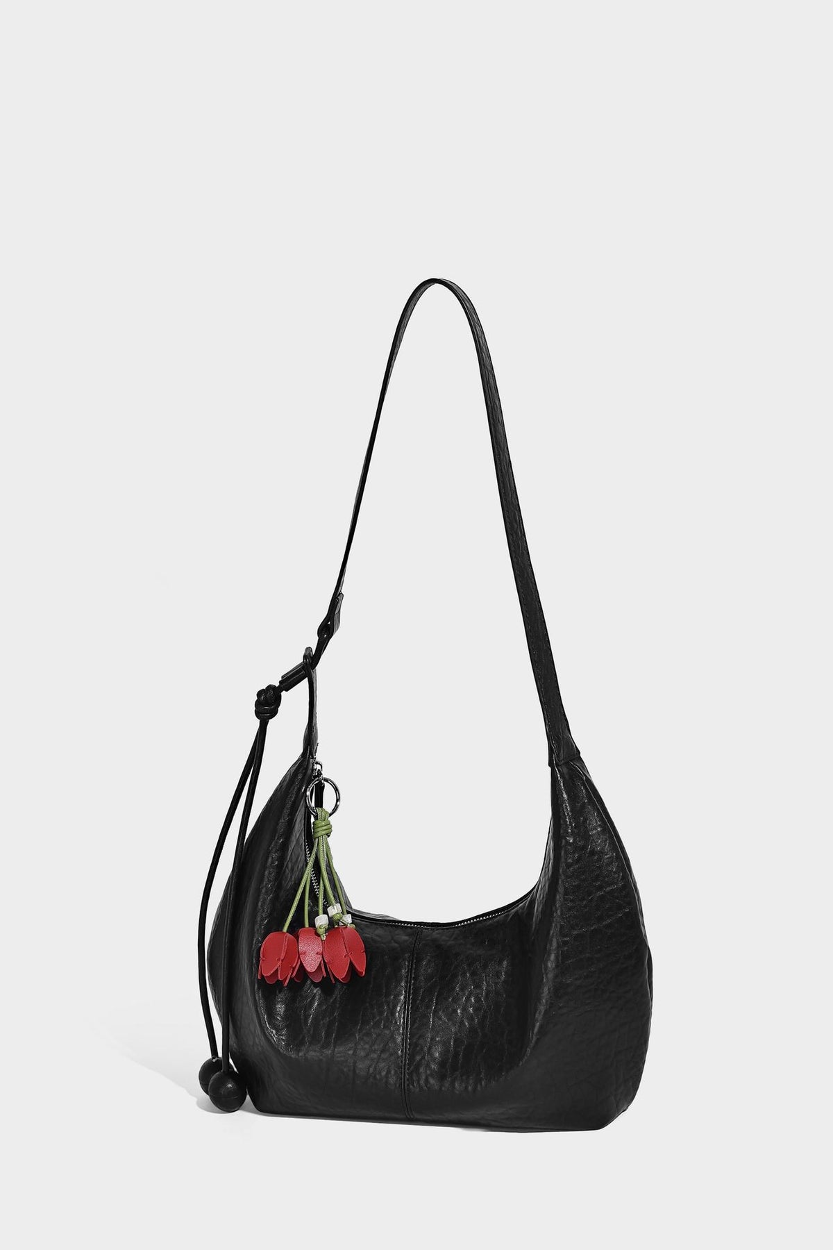 Slouchy crescent half-moon shoulder bag in pink pebbled textured finish with floral charm and knotted side detail, detail