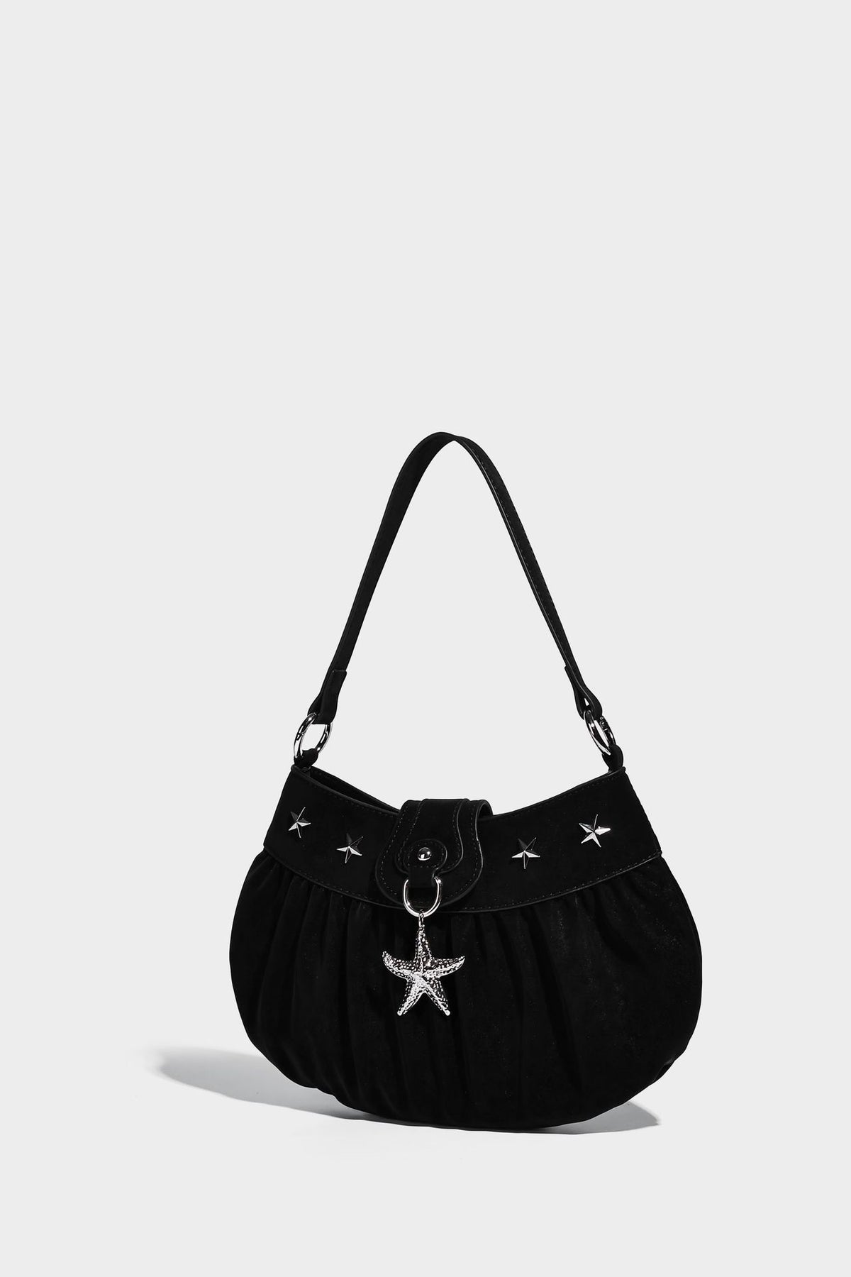 Ruched shoulder bag with curved flap, silver star studs, dangling starfish charm, and adjustable crossbody strap, detail view