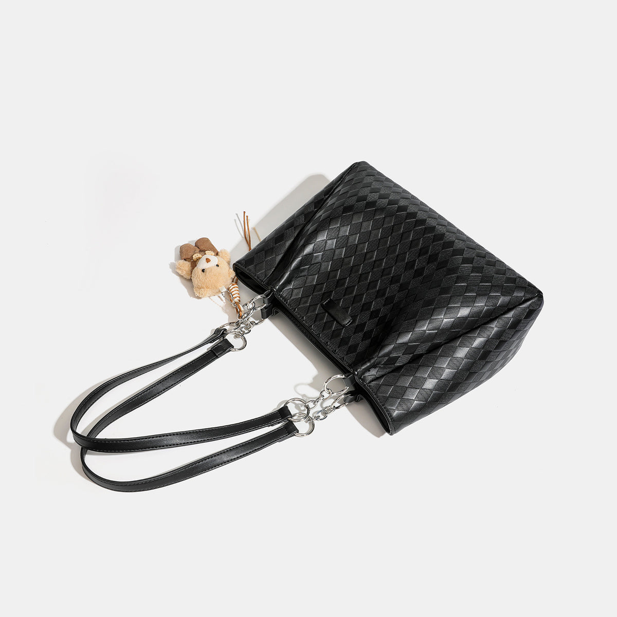 Black diamond-quilted leather-look tote bag with silver chain-ring shoulder straps and plush bear charm pendant, detail view