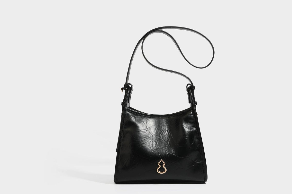 Strukturierte, trapezförmige Schultertasche aus glänzender, geknautscht wirkender Lederoptik mit goldfarbenen Beschlägen auf der Vorderseite und langem, verstellbarem