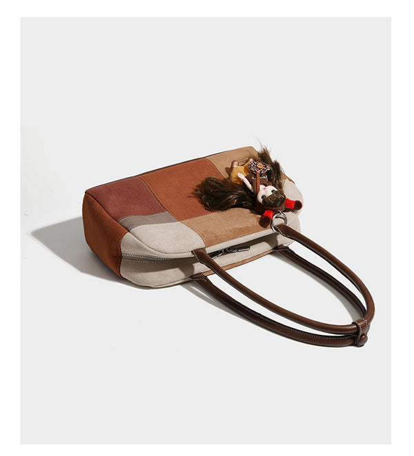 Boxy patchwork suede-look shoulder tote in tan, beige, rust, and brown panels with double brown straps and hanging doll
