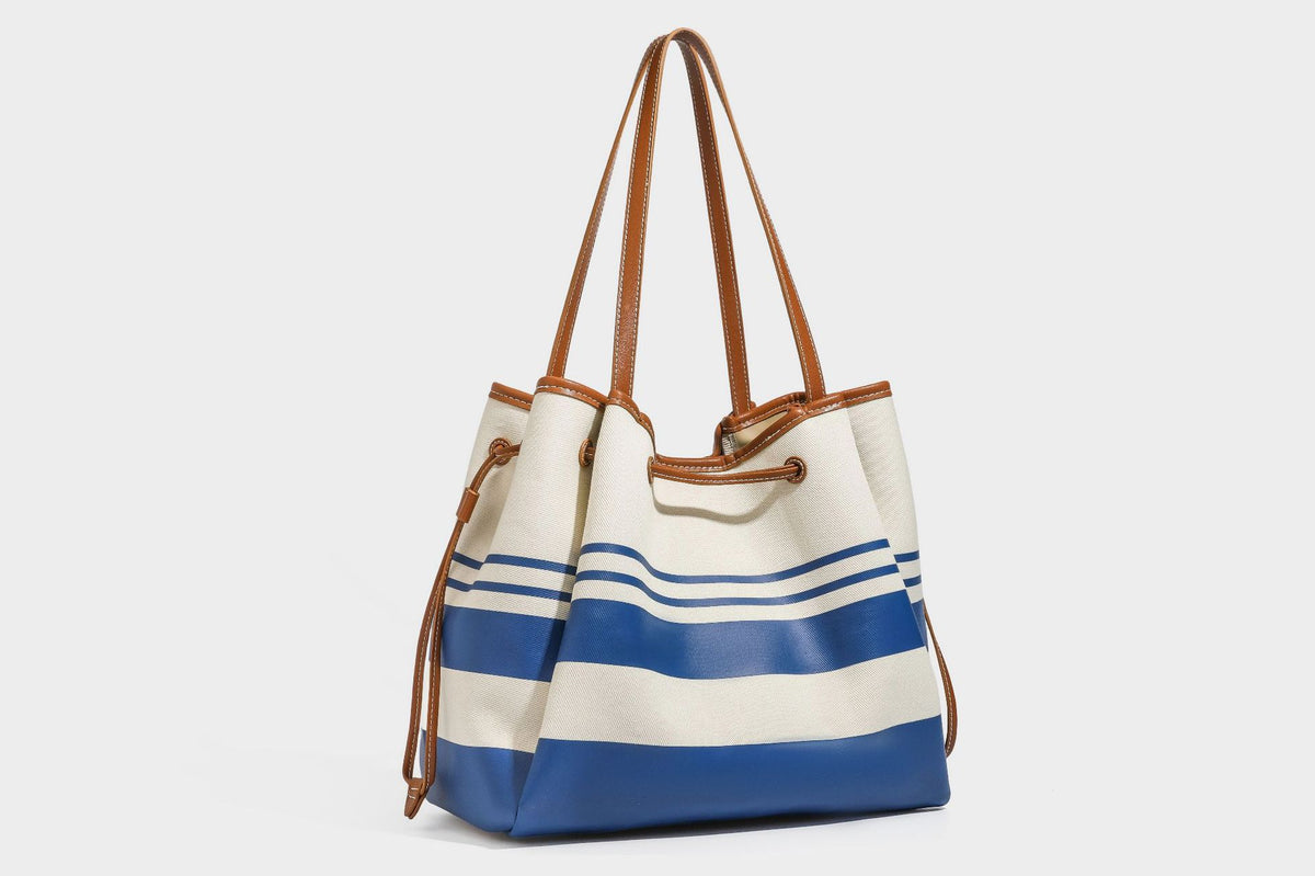 Large cream and navy striped canvas bucket tote bag with tan leather-look trim, drawstring closure, and double shoulder