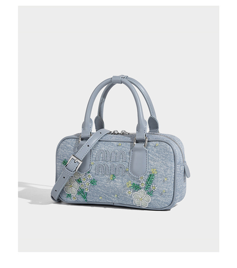 Small light blue denim-look barrel bag with white floral bead embroidery, dual top handles, and detachable shoulder strap