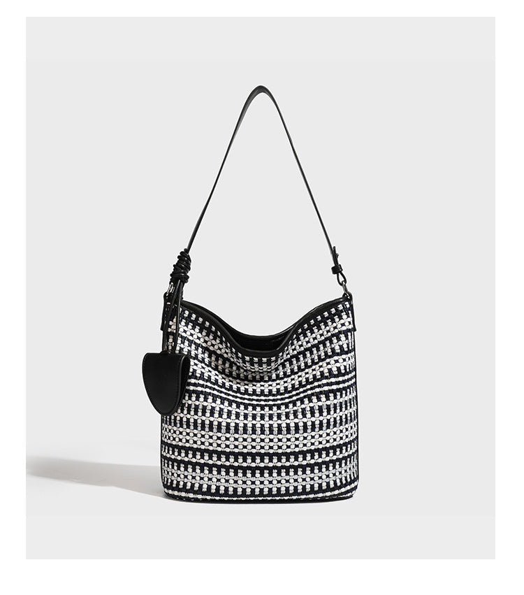 Woven stripe bucket shoulder bag in cream and dark brown with leather-look trim, knotted adjustable strap, and small shield