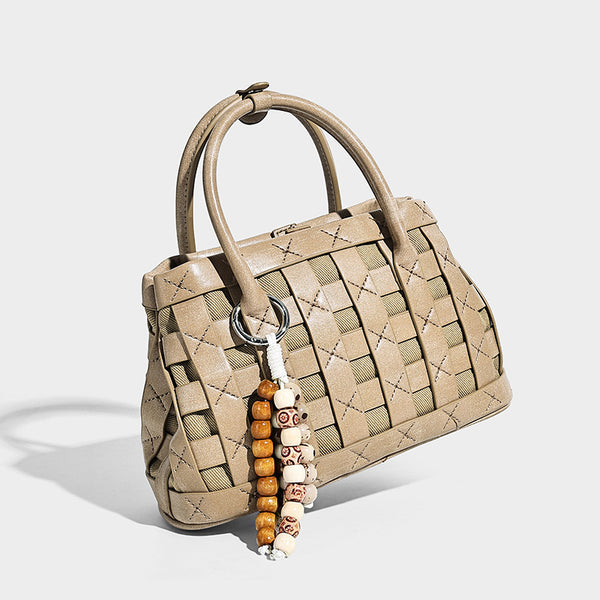 Small structured woven satchel tote with rounded top handles, silver-tone ring hardware, and bead tassel charm, detail view