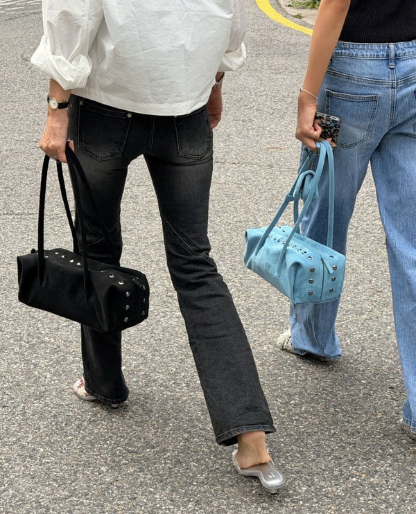 Rechteckige, zylinderförmige Schultertasche mit kuppelförmigen Nieten in Gunmetal-Optik entlang der oberen Naht, zwei flachen Riemen mit Knotendetail und matter Oberfläche, Detail