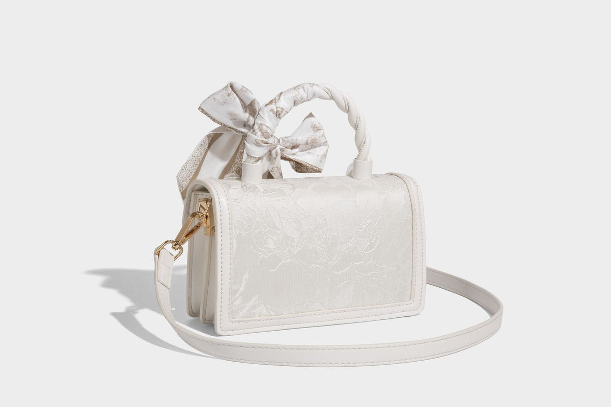 Small structured white flap bag with butterfly embroidery, flower-shaped turn-lock clasp, braided top handle with scarf bow