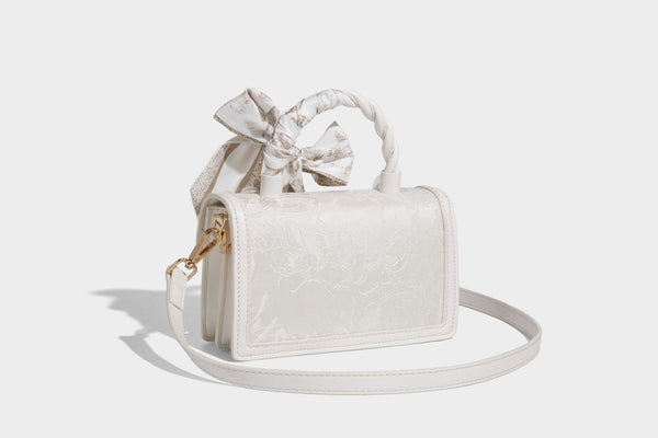 Small structured white flap bag with butterfly embroidery, flower-shaped turn-lock clasp, braided top handle with scarf bow