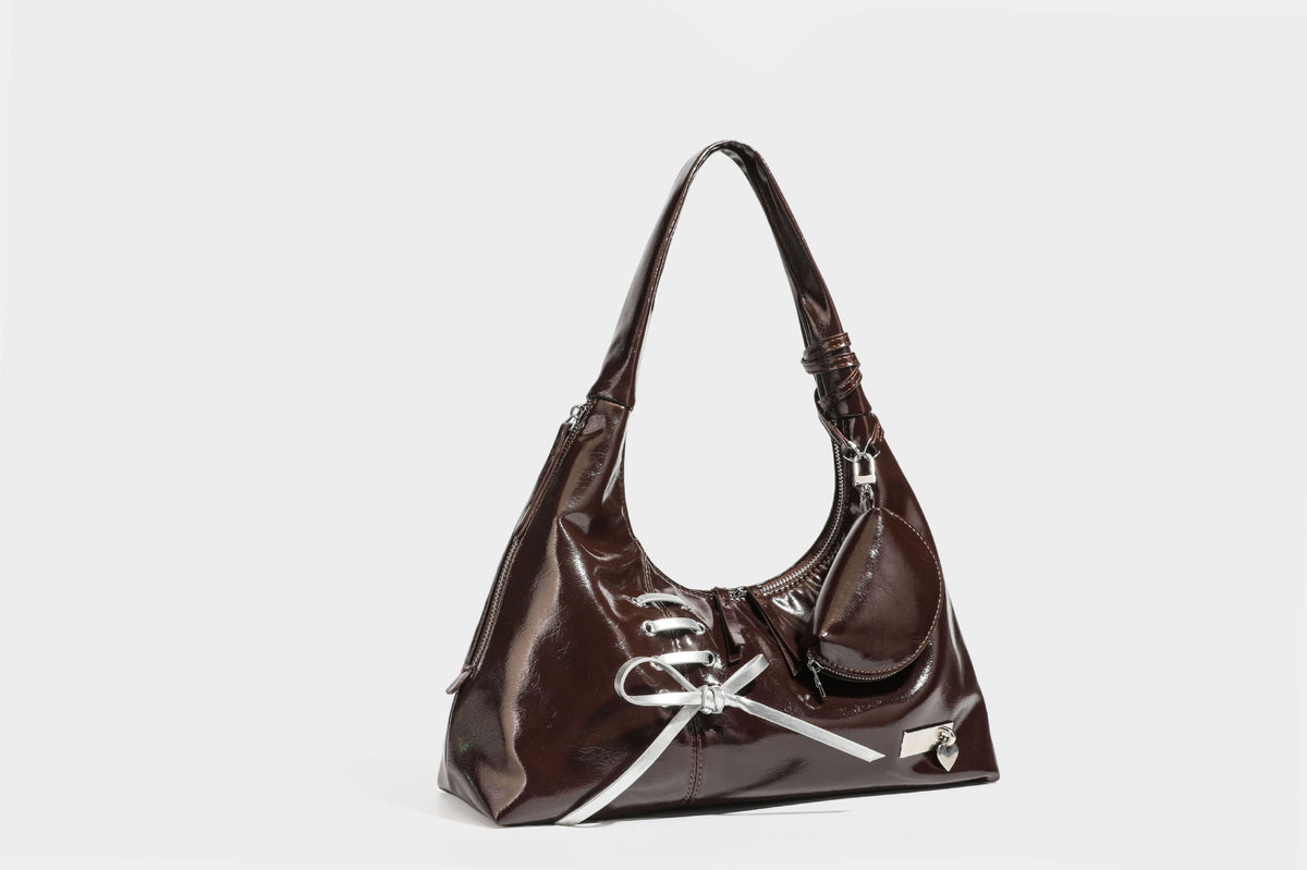Weich fallende Hobo-Schultertasche in glänzender Lederoptik mit silberfarbenen Ösen zum Schnüren und Schleifenband auf der Vorderseite, Detailansicht