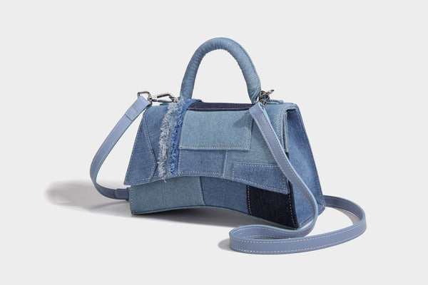 Structured patchwork denim trapezoid satchel bag with frayed panel trim, rounded top handle, and silver-tone hardware, detail