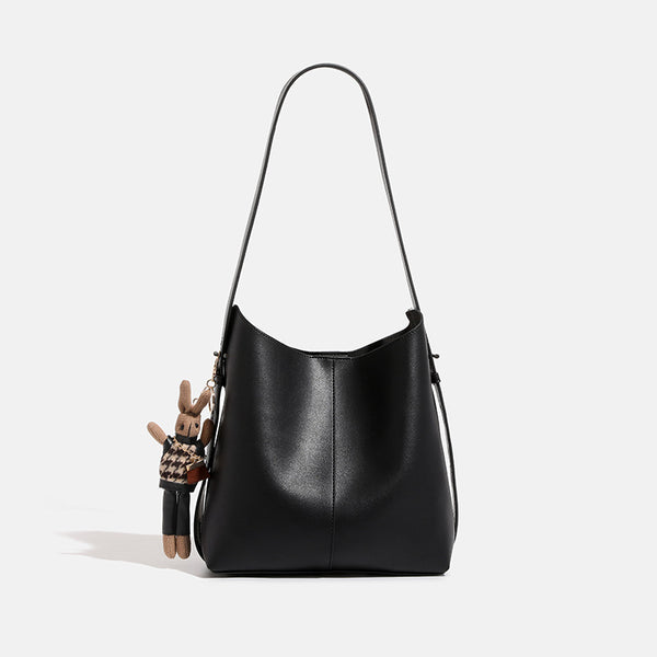 Smooth leather-look bucket bag with long flat shoulder strap, open top, gold-tone hardware, and decorative rabbit charm