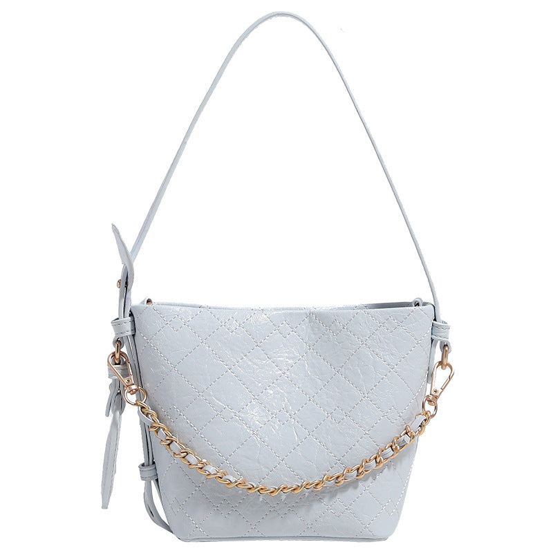 Small diamond-quilted bucket bag with gold-tone chain accent, heart strap detail, hanging tag, and matching zip coin pouch