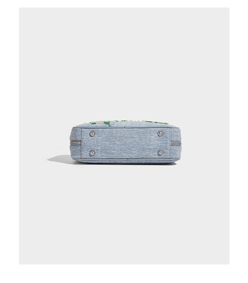 Small structured light blue denim-texture bowling bag with white floral bead embroidery, dual rounded top handles, and