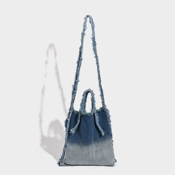 Washed denim fringe crossbody bag with indigo-to-pale-blue gradient and raw fringe trim along edges and shoulder strap