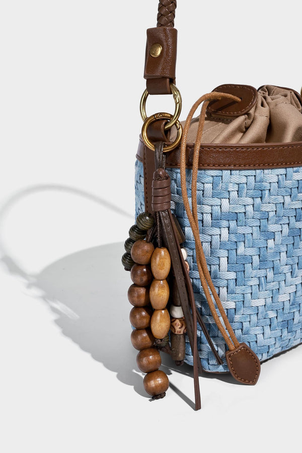 Small light blue woven bucket bag with brown leather-look trim, braided top handle, brass-tone ring hardware, drawstring