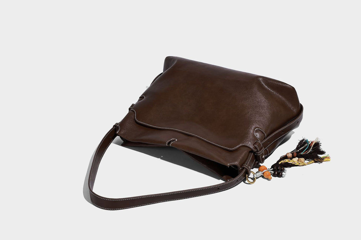 Large slouchy leather-look hobo tote bag with open top, adjustable shoulder strap, and colorful tassel bead charm, detail
