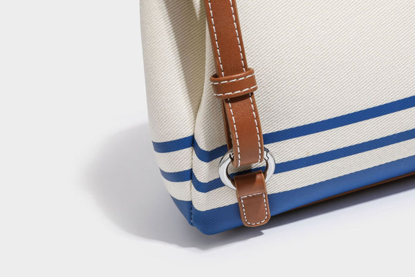 Cream canvas bucket bag with blue horizontal stripes, tan leather-look flap and trim, drawstring closure, silver-tone, detail