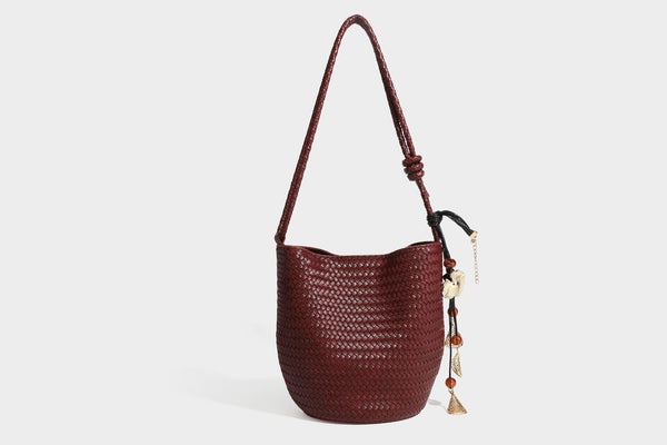 Olive green woven leather-look bucket bag with braided crossbody strap, knotted adjustment, and gold-tone tassel charm with